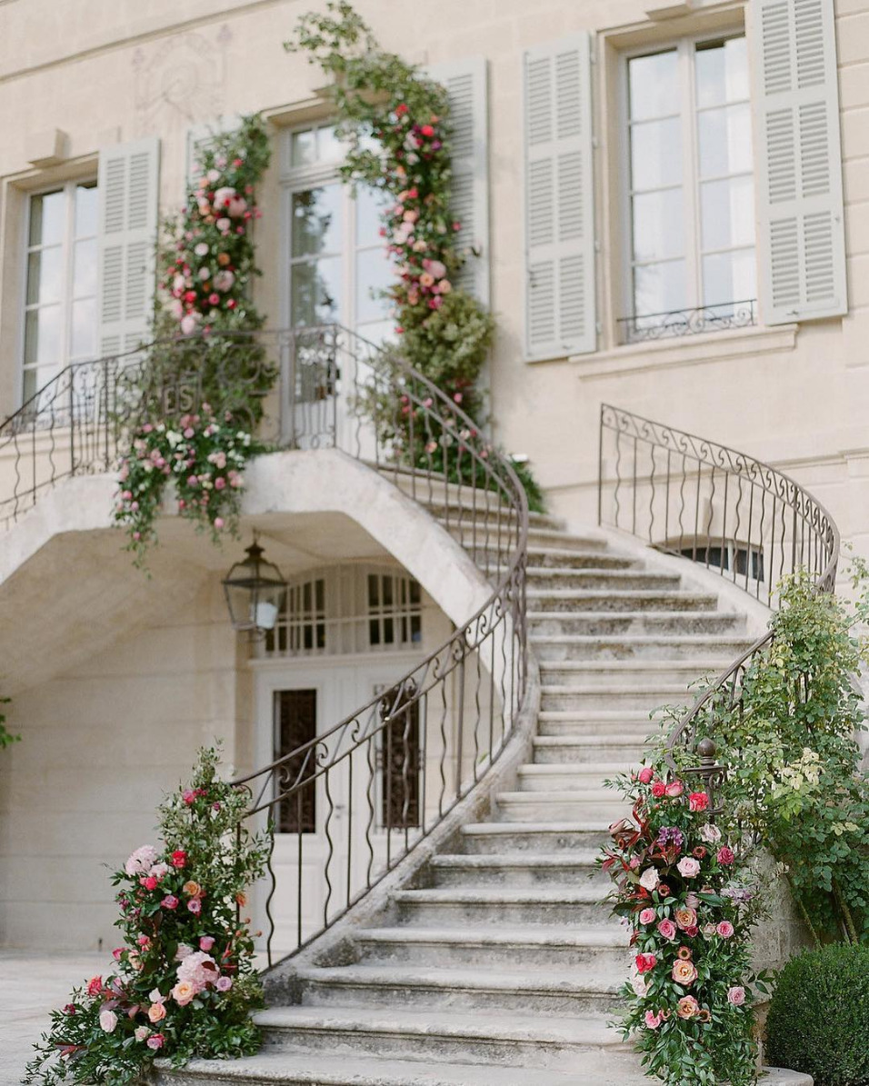 Classic curved stone staircase leading to glass door with wedding flowers running up the handrail.