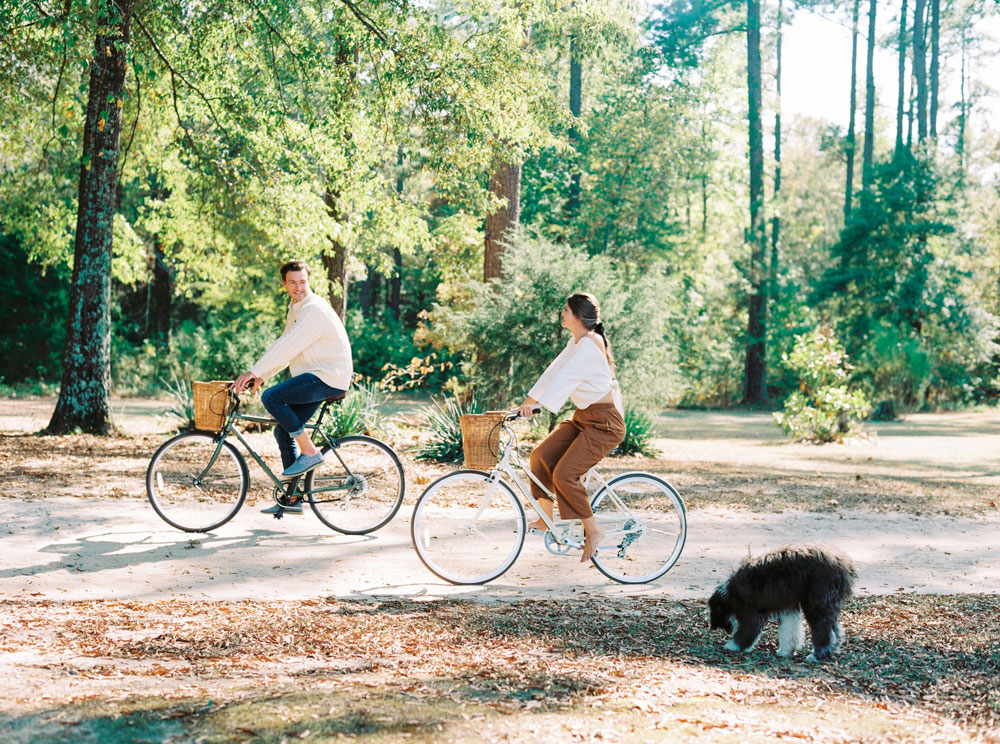 Engaged couple riding bikes in the woods with their Sheepadoodle