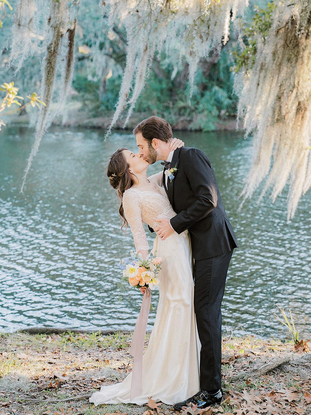 Bride and groom kissing underneath a willow tree next to the lake at Legare Waring House, Charleston SC