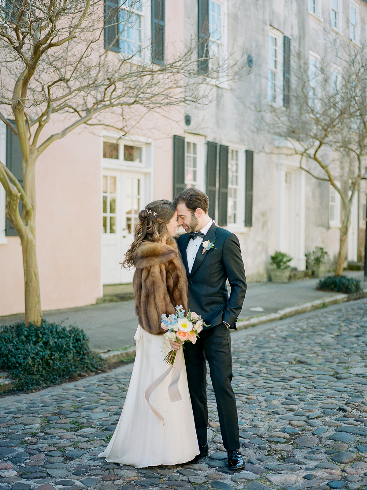 pastel building cobblestoned street wedding portraits with bride in a vintage inspired gown and groom in a black tux