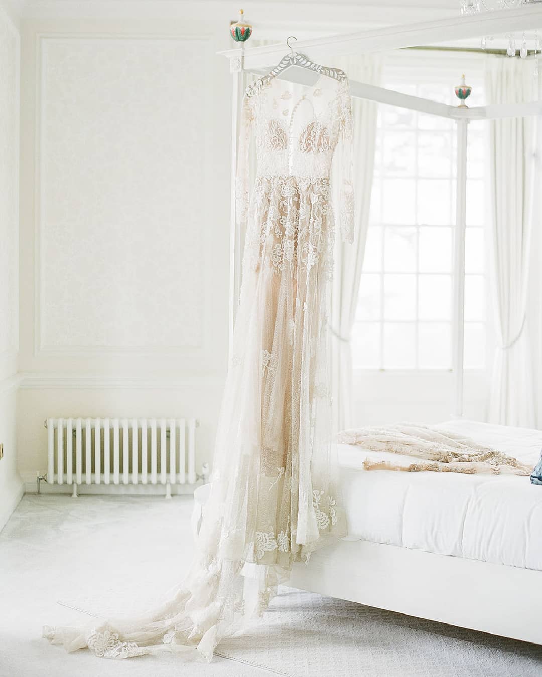 luxury wedding dress with lace embroidery hanging from a canopy bed at an English manor house wedding venue