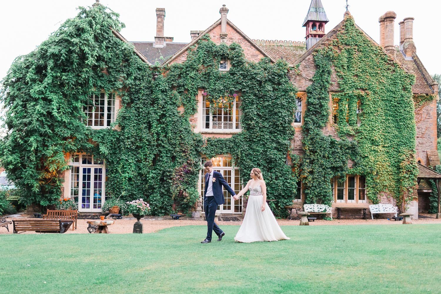 Bride and groom walking hand in hand outside an ivy-covered manor house in the English countryside 