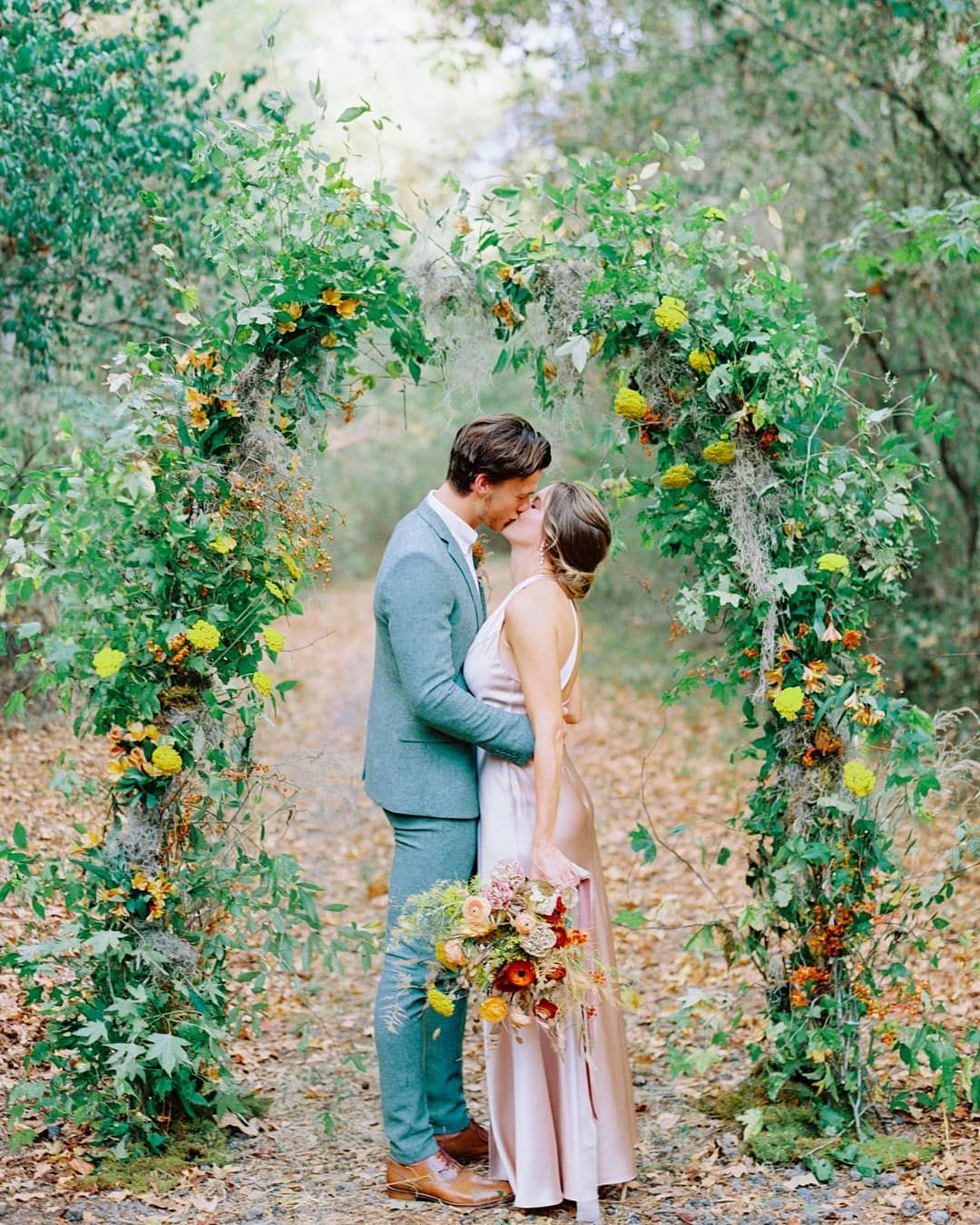 woodsy wedding ceremony witha greenery and seasonal flower arch and couple kiss