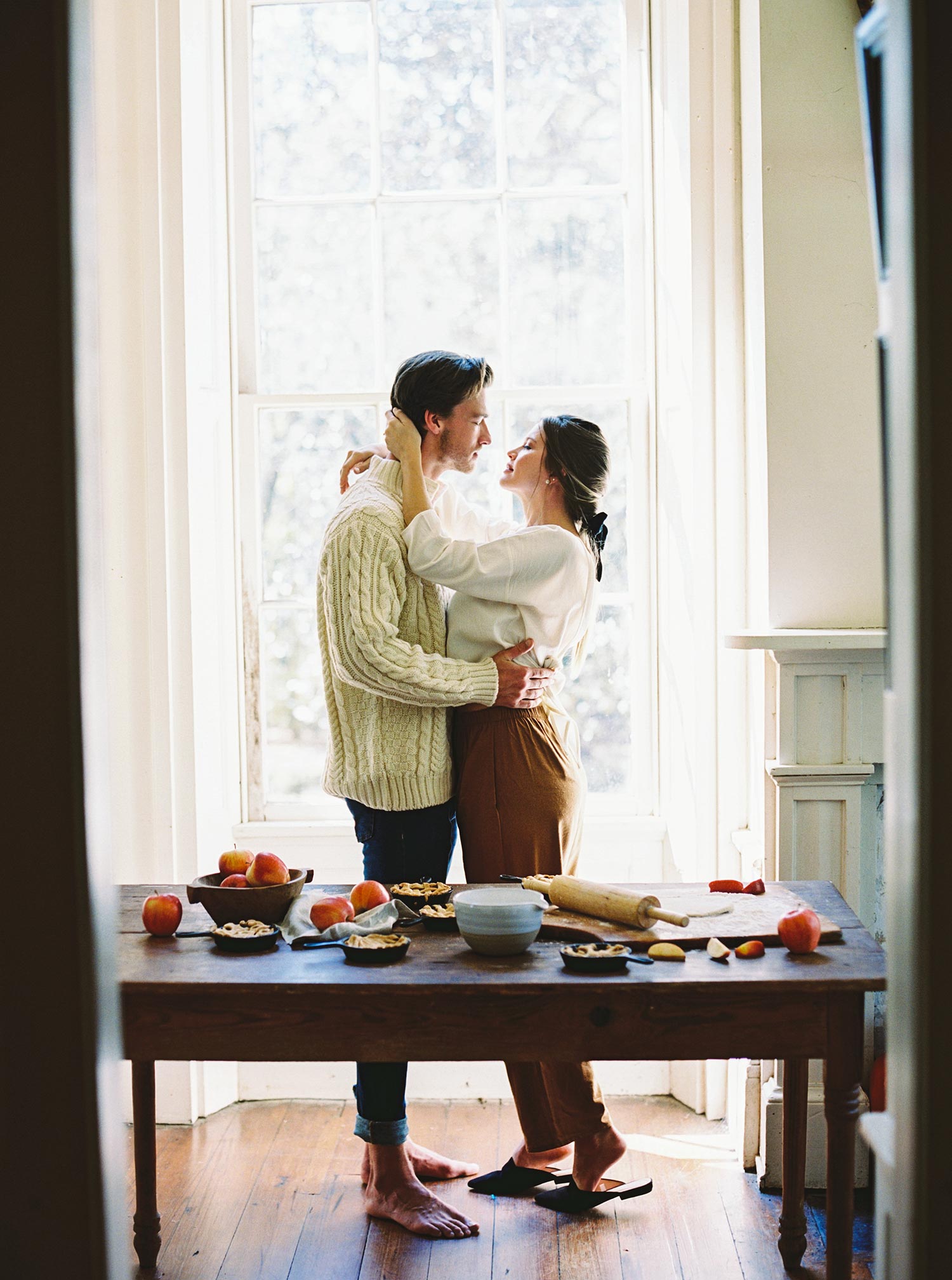 white linen blouse with rust colored pants and a fisherman sweater next to homemade apple pie station for a cozy autumn date night idea