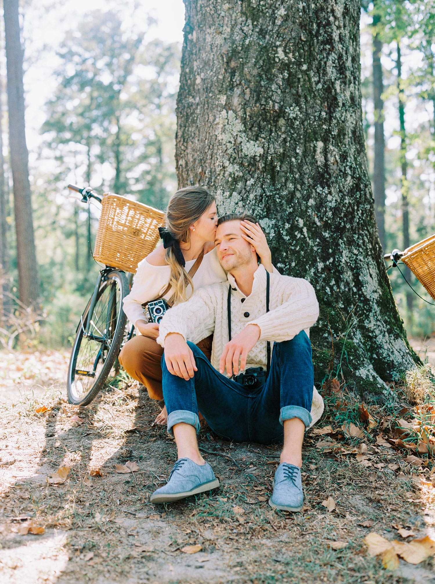 white linen blouse with rust colored pants and a fisherman sweater rest their bicycles on an old tree during autumn for a fall date idea