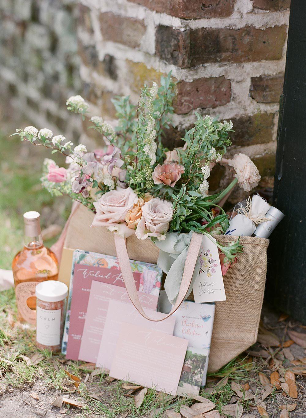 burlap tote with flowers, bath salts, champagne, chocolates and a modern weekend itinerary for a destination wedding welcome bag in Charleston, SC at Middleton Place; photography by The Happy Bloom and planning by Willow and Oak Events