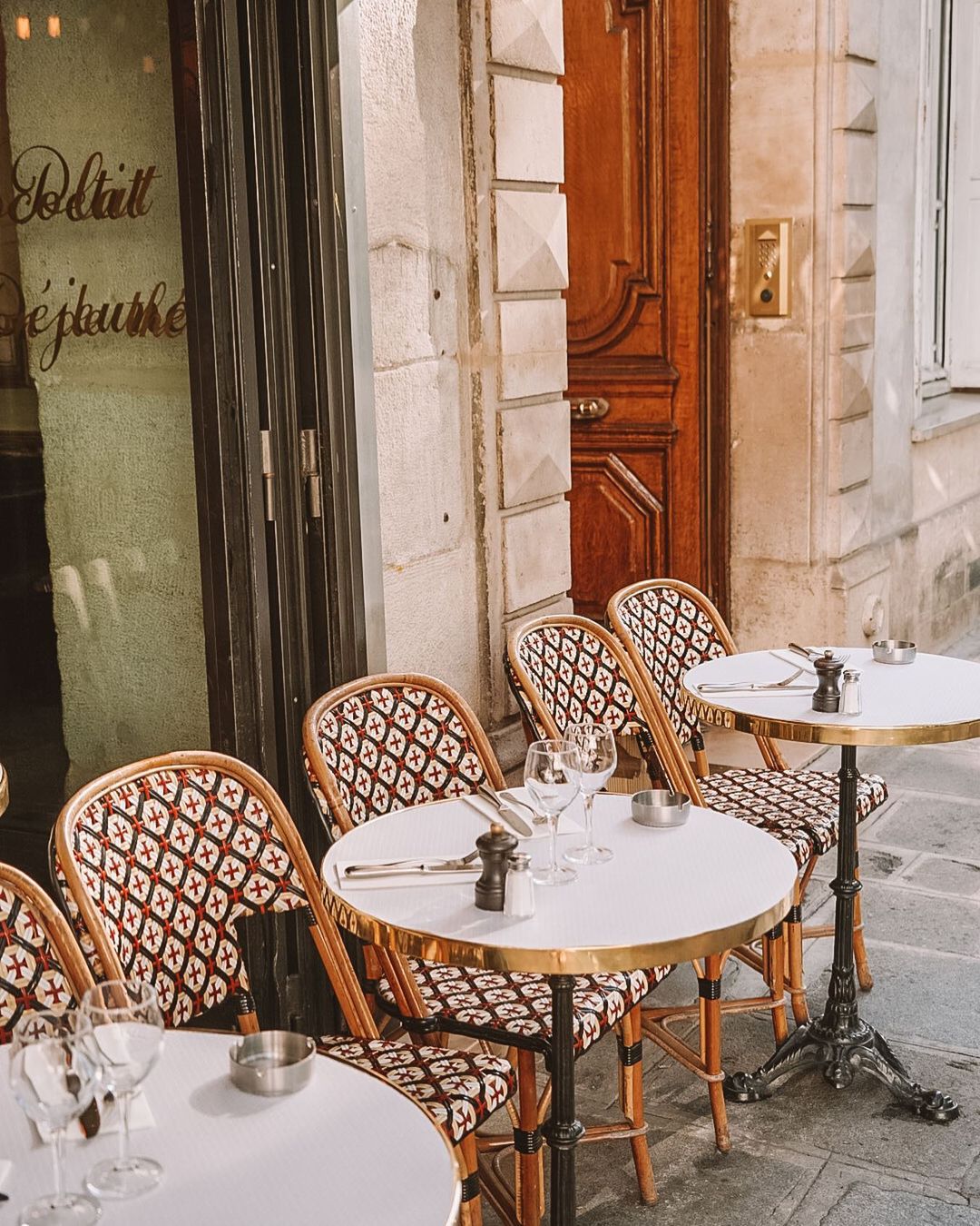 Parisian cafe seating with marble bistro tables and rattan chairs facing out at the streets for people-watching