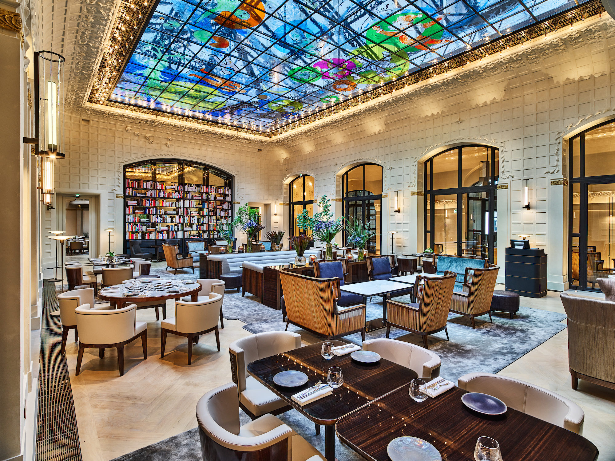 The interiors of Le Saint-Germain restaurant at Hotel Lutetia with custom woven raffia armchairs and outlandish watercolor motifs painted onto the large glass ceiling
