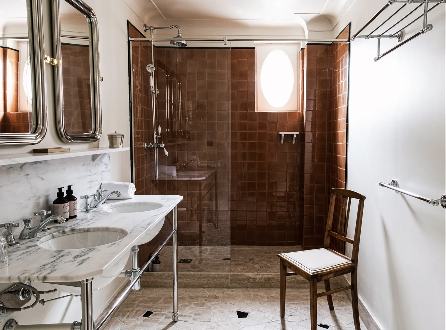 A glossy leather brown tile for a walk-in shower beside a white marble double-sink at Hotel Rochechouart