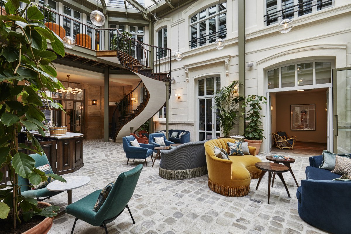 Mid-century modern velvet furniture in the lobby of The Hoxton Paris with a grand spiral staircase