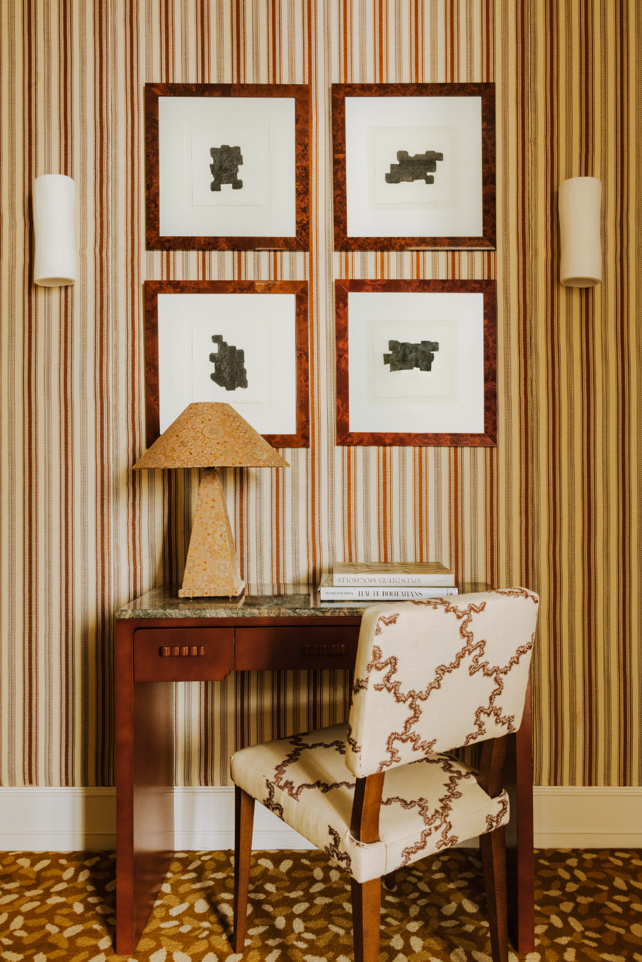 A designer writing disk with a mahogany wood base and green marble surface staged against a striped wallpaper gallery wall and accented with a squiggly patterned desk chair and allover cork table lamp