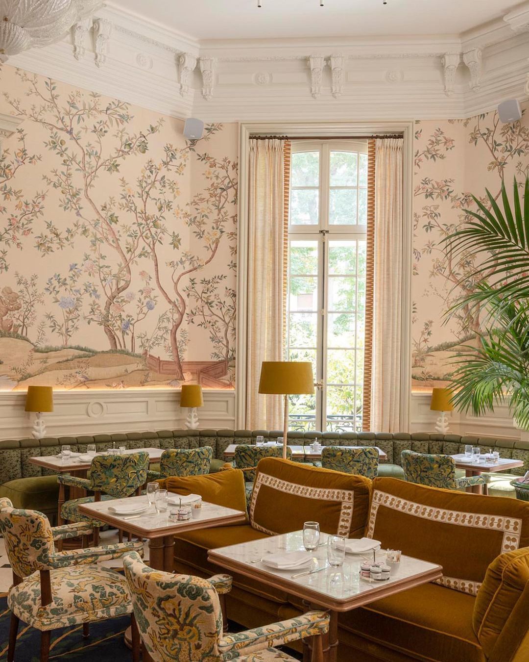A winter-garden ambiance blurs the indoor-outdoor line: delicately drawn panoramas, moldings, woodwork, black and beige tiling, a period fireplace beneath an ancient mirror that reflects the greenery of the outdoor garden, Auduze pottery vases planted with kentia, a bird or two flitting by...
