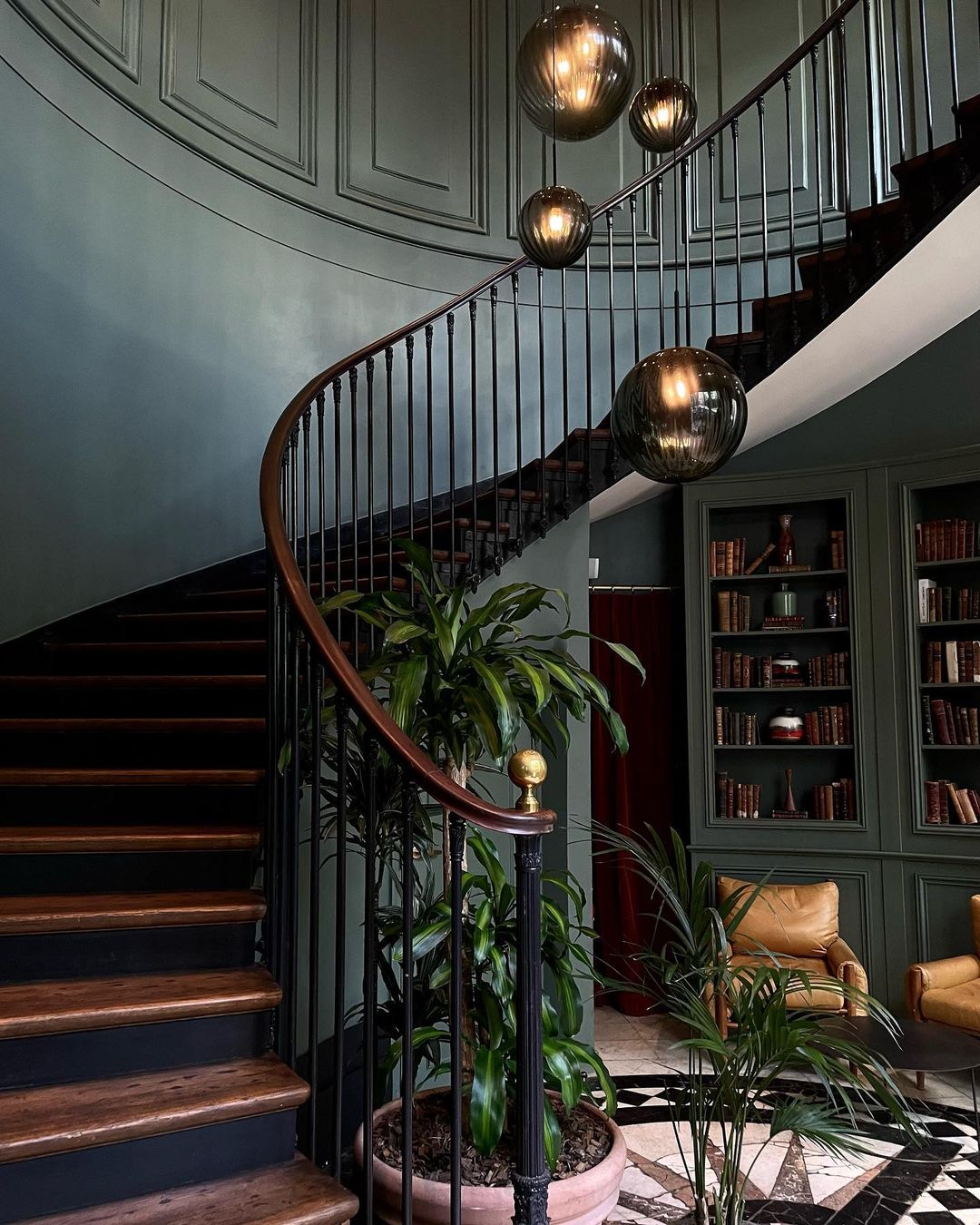 A forest green foyer with an 18th c spiral staircase and leather arm chairs at The Hoxton Paris