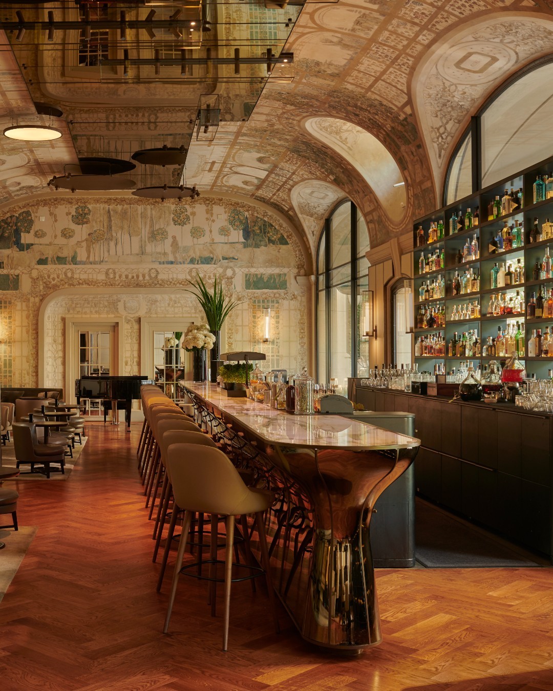 The interiors of Bar Josephine at Hotel Lutetia in Paris with curved double-height ceilings, painted floor-to-ceiling murals and a copper + marble bar