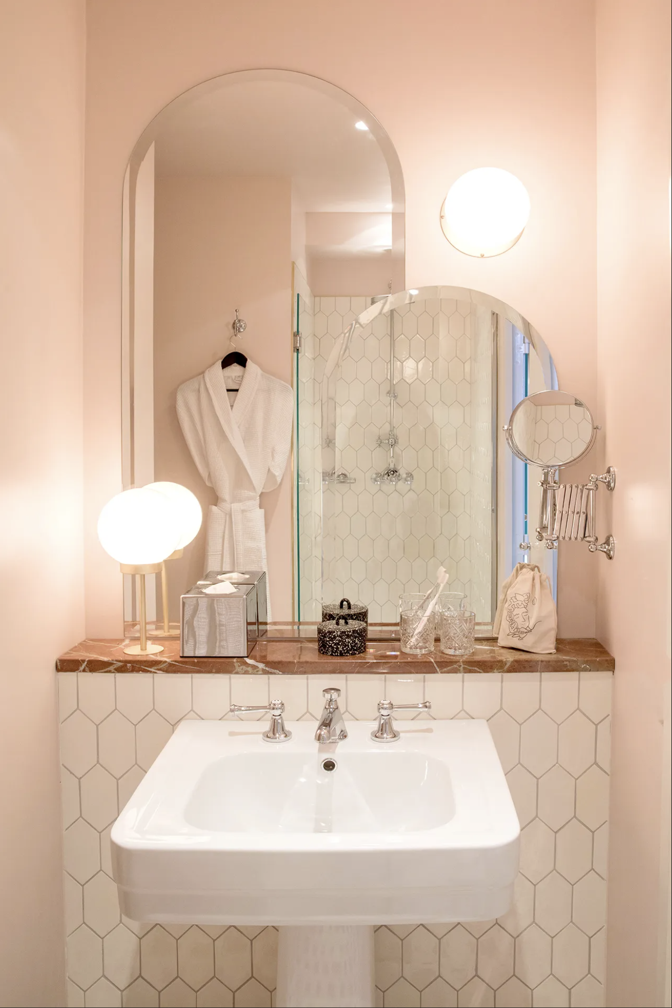 A pale pink bathroom with coral marble countertops, layered domed mirrors in two sizes and modern orb lighting at Hotel des Grands Boulevards