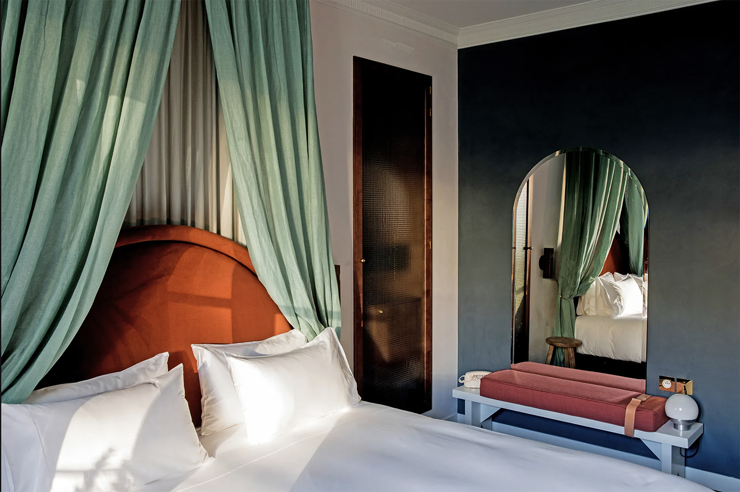 A dramatic sage linen canopy bed with a burnt orange velvet headboard and navy walls at Hotel des Grands Boulevards