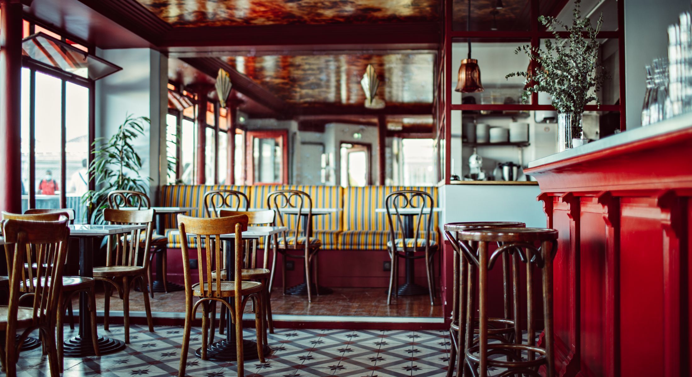 The old-school style brasserie Cafe les Deux Gares with wooden thonet chairs and bar stools, vintage floor tiles, antique mirrored walls and a red bar facade