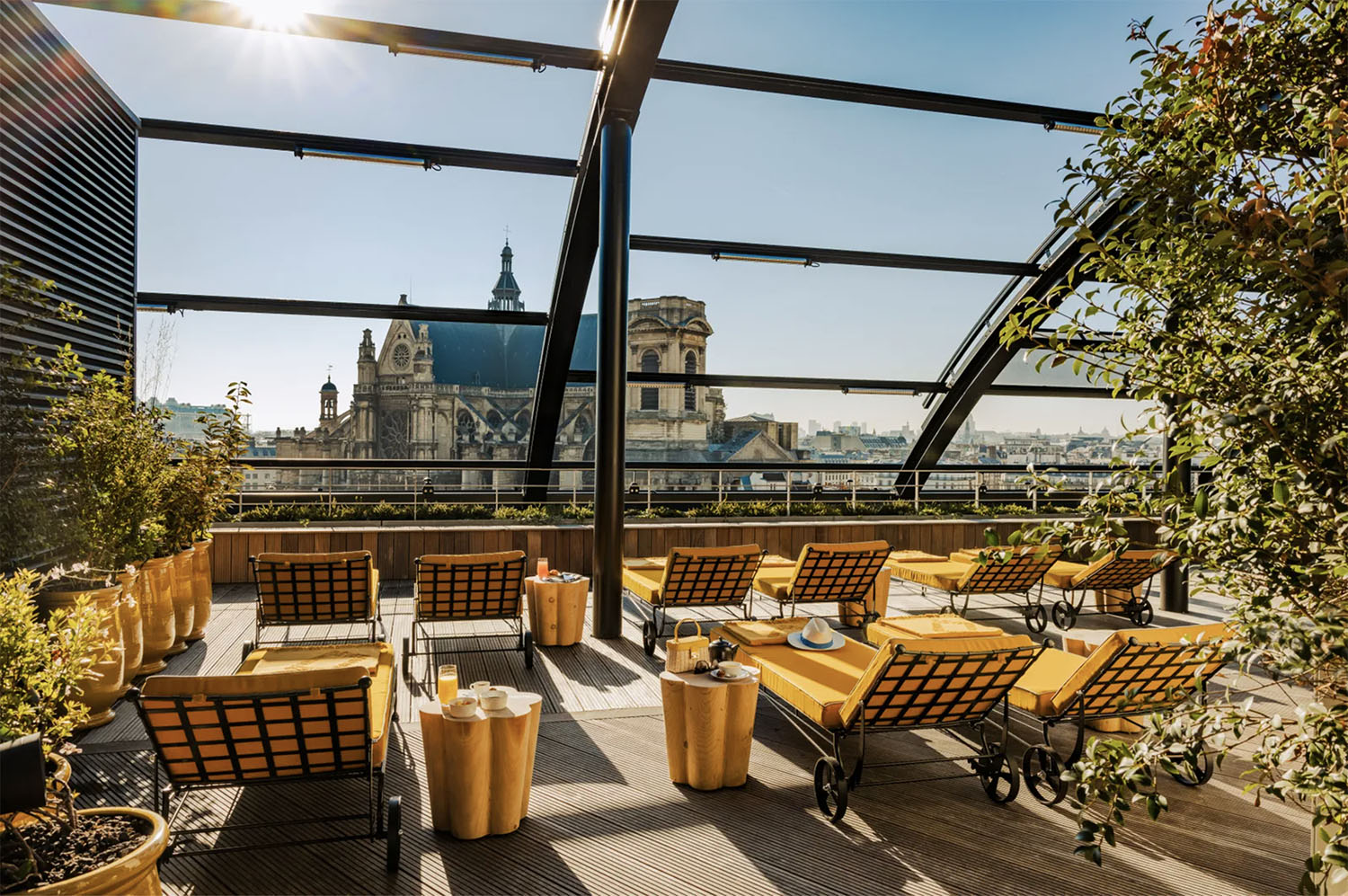 A panoramic rooftop at Hotel Madame Rêve with a retractable glass roof, yellow cushioned sun loungers and scalloped yellow side tables