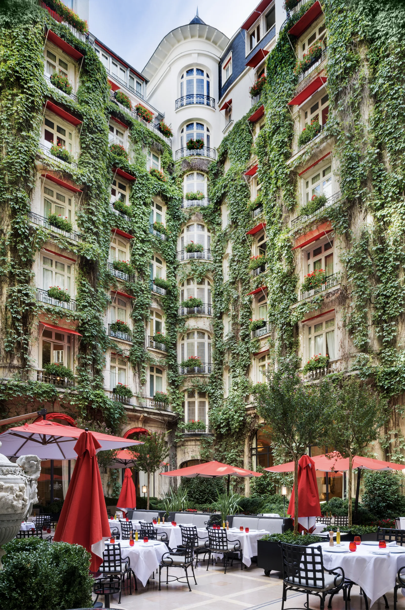 The hidden courtyard garden restaurant of Hotel Plaza Athénée with its ivy-covered walls spanning 8 stories and crisp white linen tables beneath bold red parasols