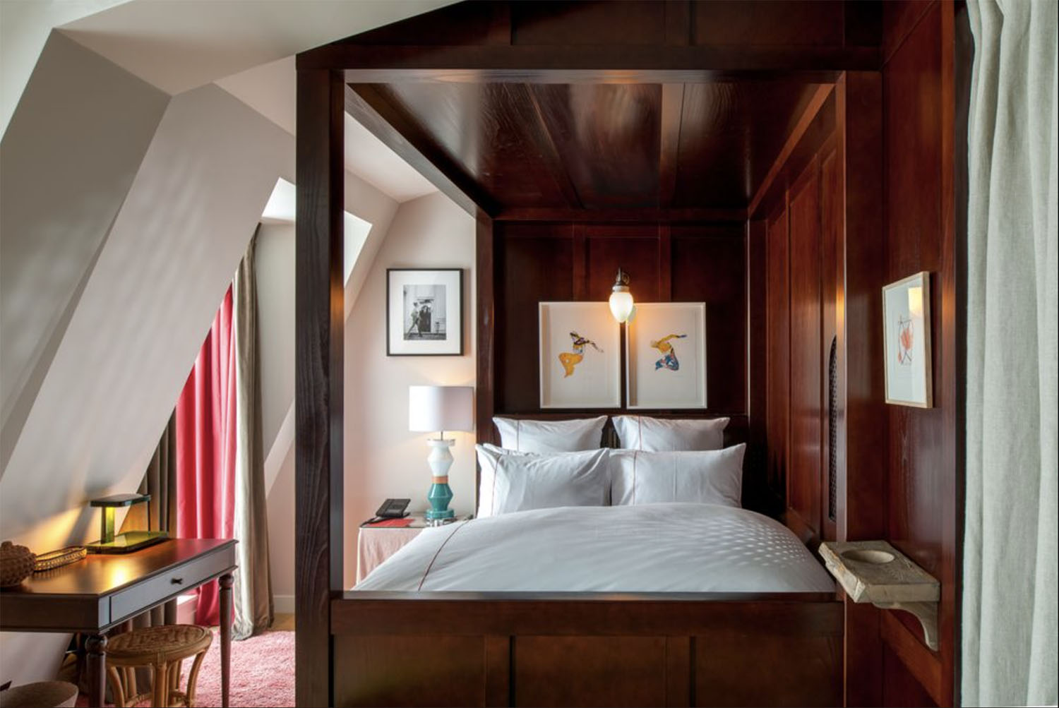 A wooden canopy bed surrounded by contemporary artwork and vaulted walls
