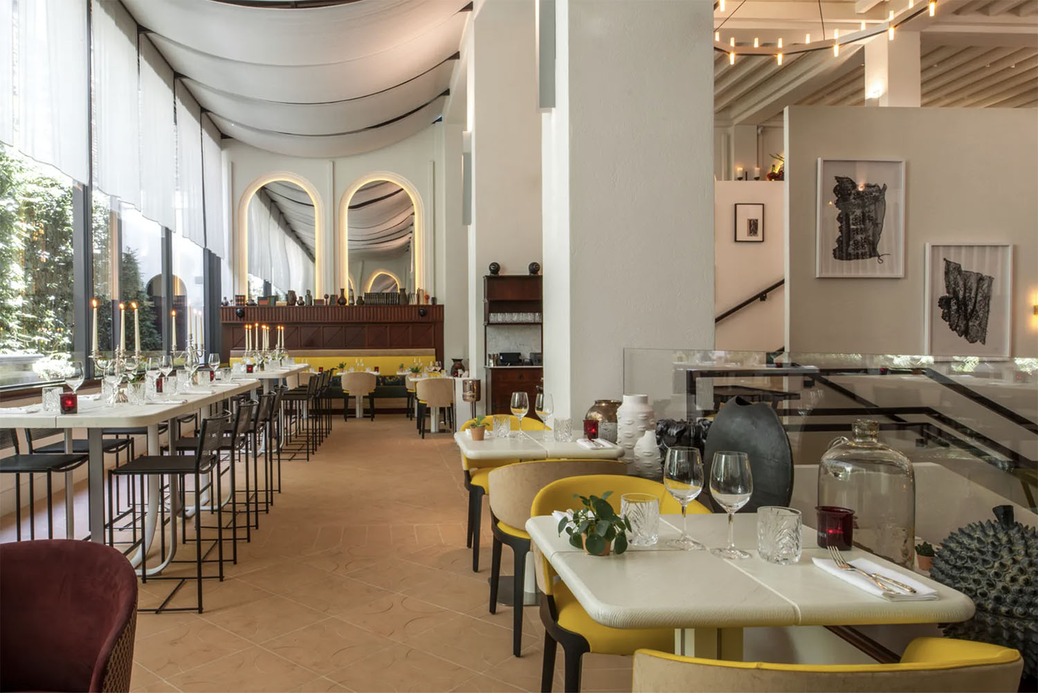 The open-air, high ceiling restaurant at Hotel Sinner with yellow chairs, white marble tables and draped panel canopies along the ceiling