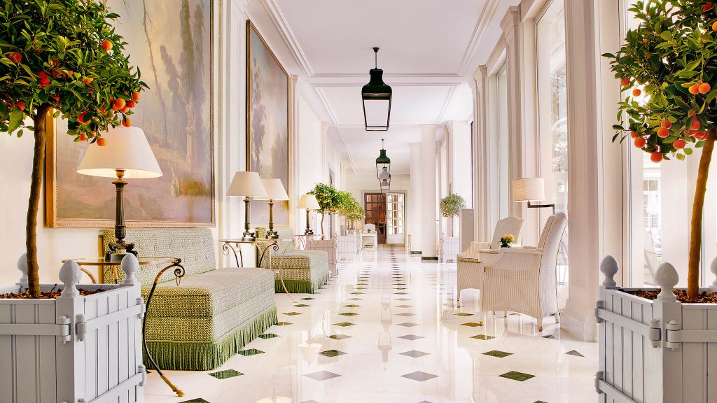 An Orangerie style corridor at Le Bristol Paris with iron pendants, checkered floors and green sofas with fringed trim