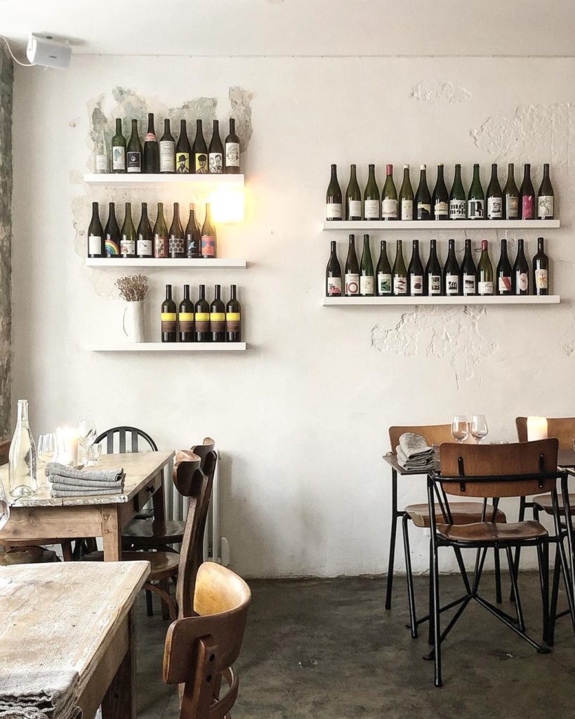 The simple Scandi style interiors of Early June with wooden school-style seating, rustic wooden tables and shelves lined with dozens of wine bottles on the walls