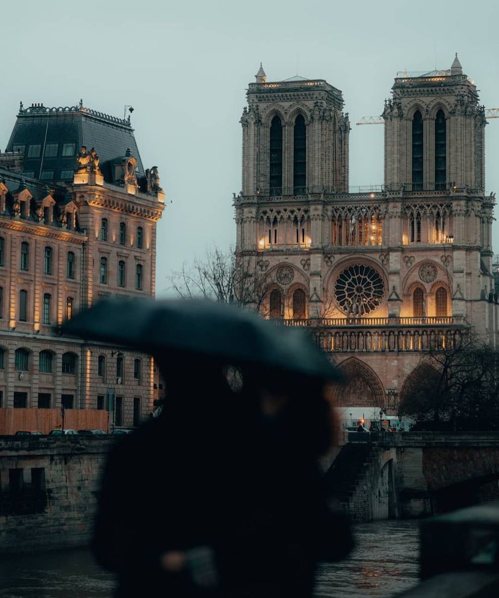 A couple admires the amber glow of the Notre Dame Cathedral on a rainy evening in Paris