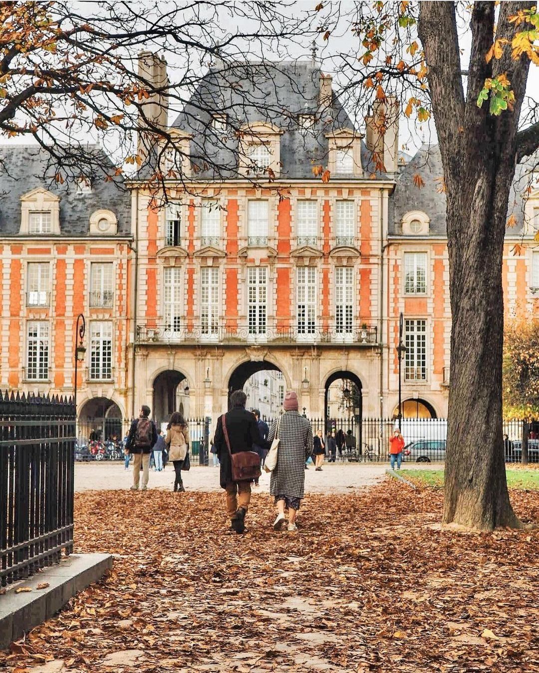 A couple walks around Place des Vosges in autumn