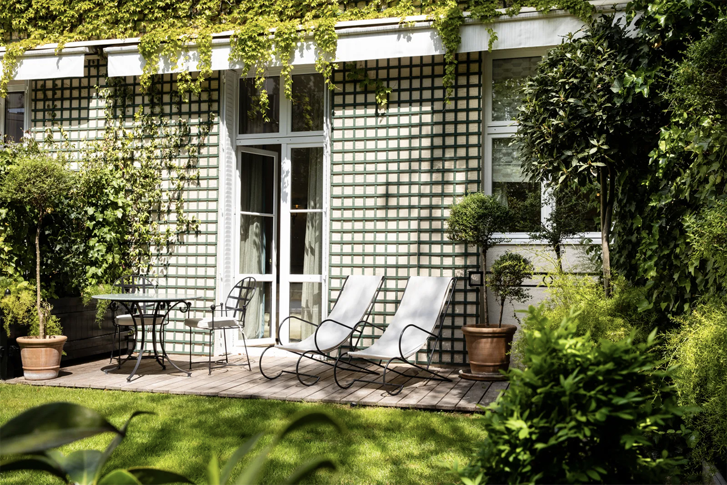 The green-latticed exterior of a Garden Suite at Relais Christine with iron + cloth deck chairs