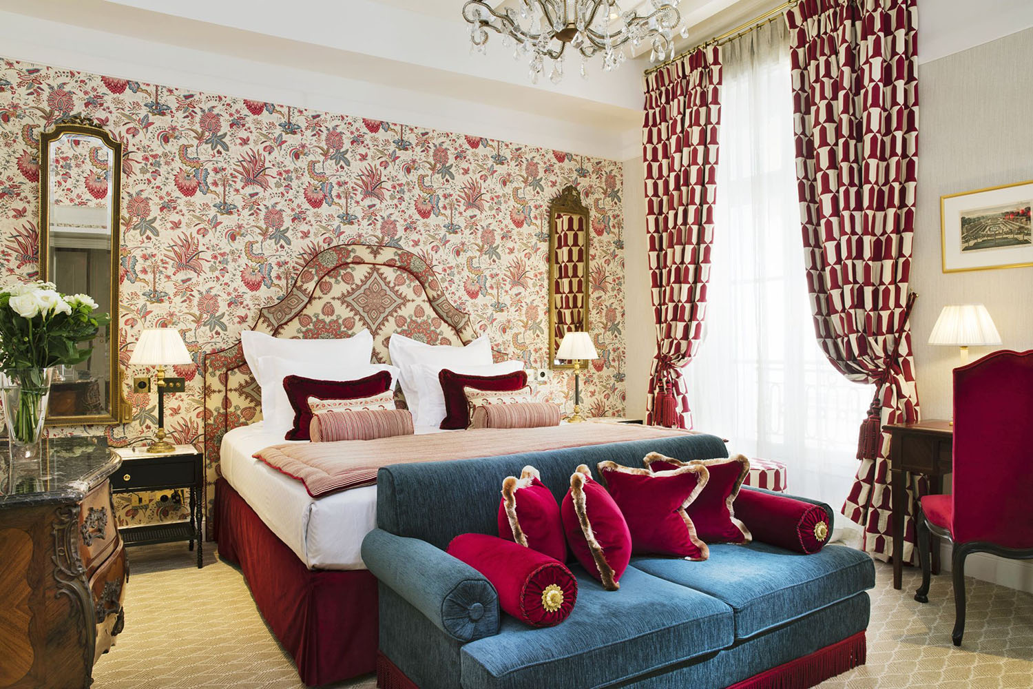 A peacock blue and ruby red room at Relais Christine with a maximalist design that layers floral chintz prints with geometric patterned curtains 