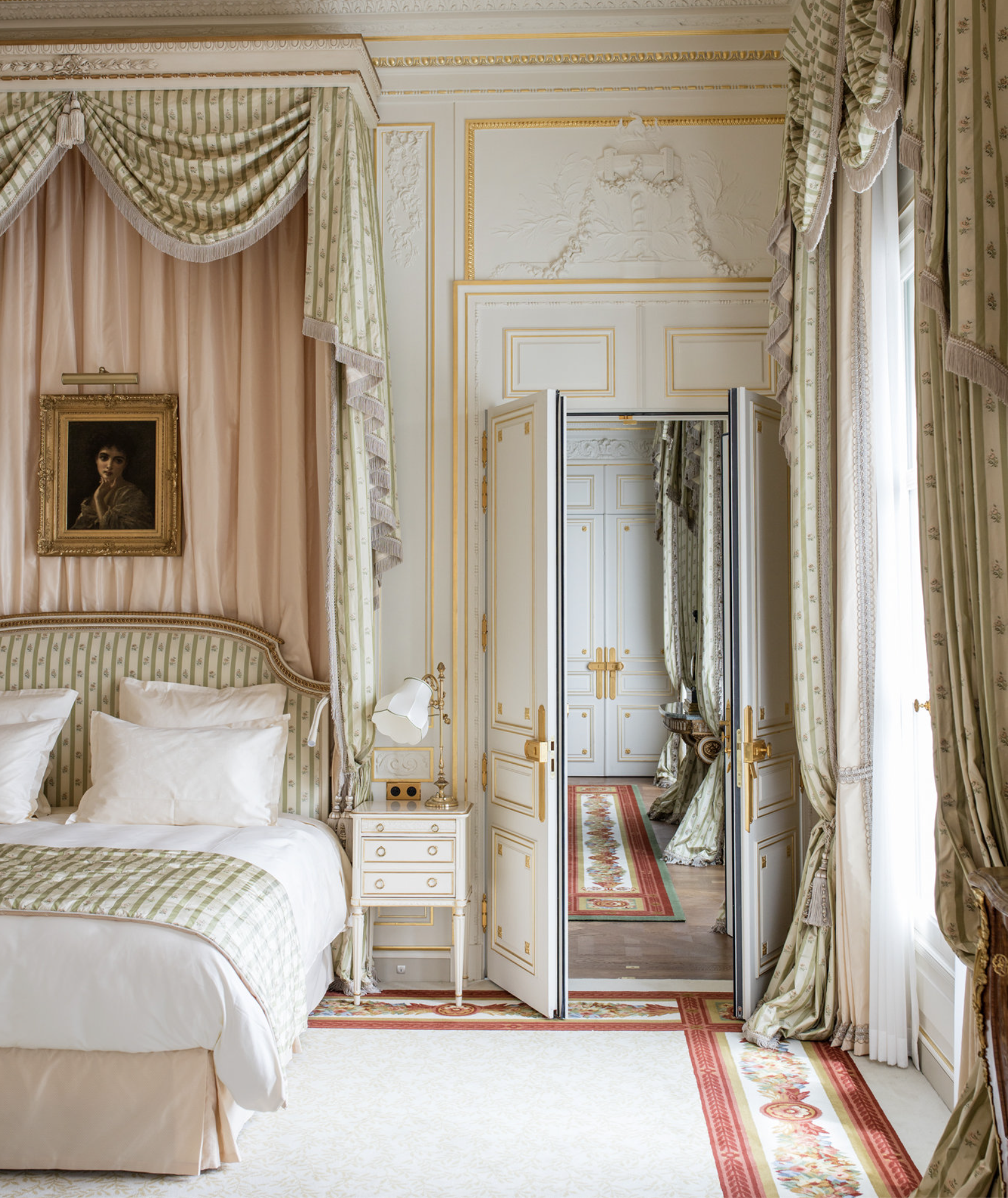 The romantic, feminine Suite Vendome at Ritz Paris with a sage, lilac and pink canopy bed inspired by Marie Antoinette, white and gold Louis XV furniture and wall paneling, floral motif curtains and floor-to-ceiling windows